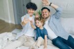Happy family mom dad and child taking selfie in bed waving hands smiling